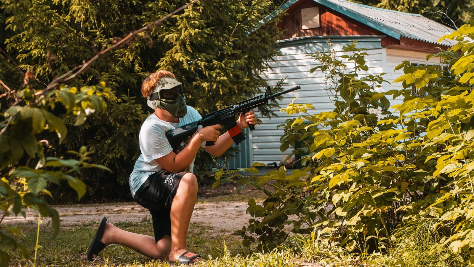 Stovyklautojas su airsoft ginklu prie stovyklos pastato